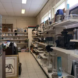Winkelinterieur met stellingen vol huishoudspullen, decoratieartikelen en diverse goederen langs de wanden en in het midden v