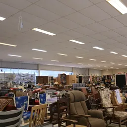 Ruim interieur van kringloopwinkel met diverse meubels, stoelen en huishoudartikelen uitgestald onder LED-verlichting