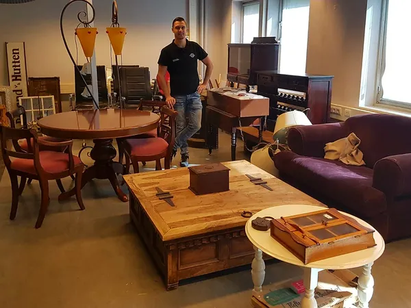 Winkelvloer met meubels: ronde tafel met stoelen, houten salontafel, paarse bank en diverse kasten. Een medewerker staat in h