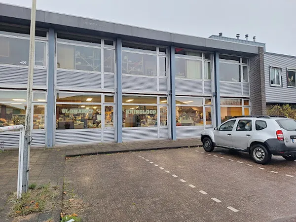 Gevel van kringloopwinkel met grote ramen en witte zonwering, witte auto geparkeerd ervoor