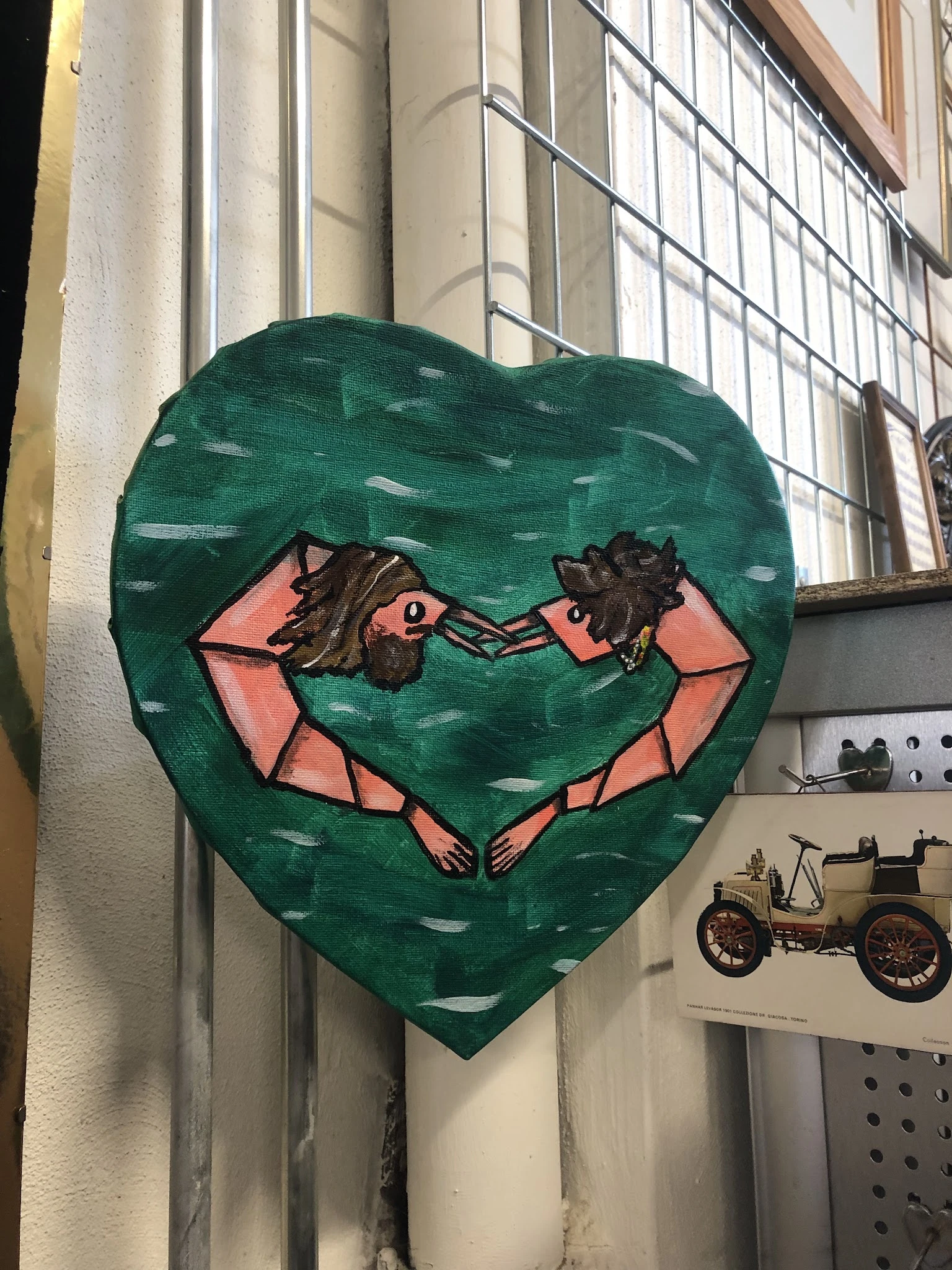 Groen hart-vormig kunstwerk met roze figuren, opgehangen aan een muur