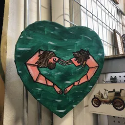 Groen hart-vormig kunstwerk met roze figuren, opgehangen aan een muur