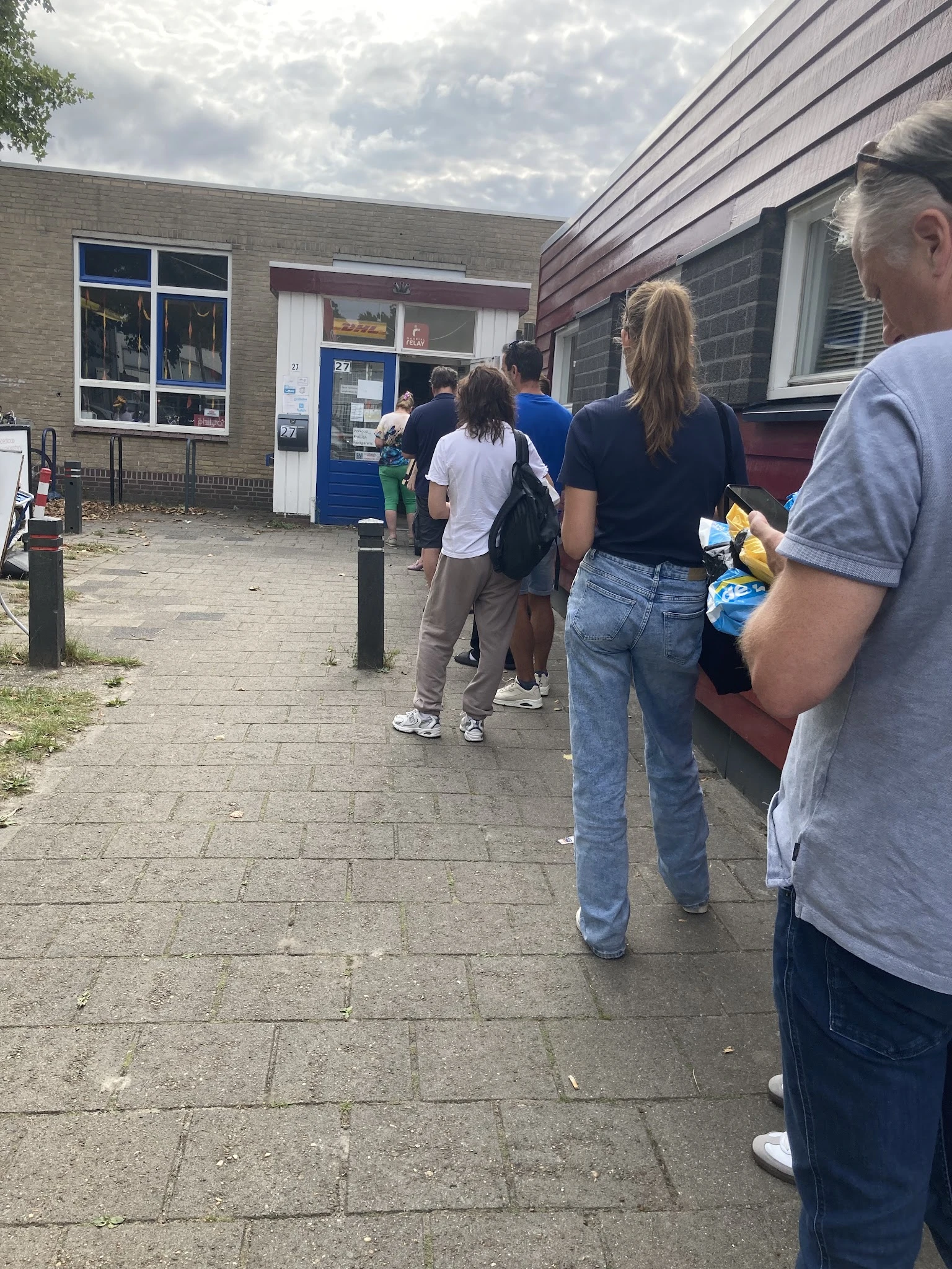 Groep mensen staat in de rij voor de ingang van een kringloopwinkel aan de straat