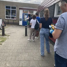 Groep mensen staat in de rij voor de ingang van een kringloopwinkel aan de straat