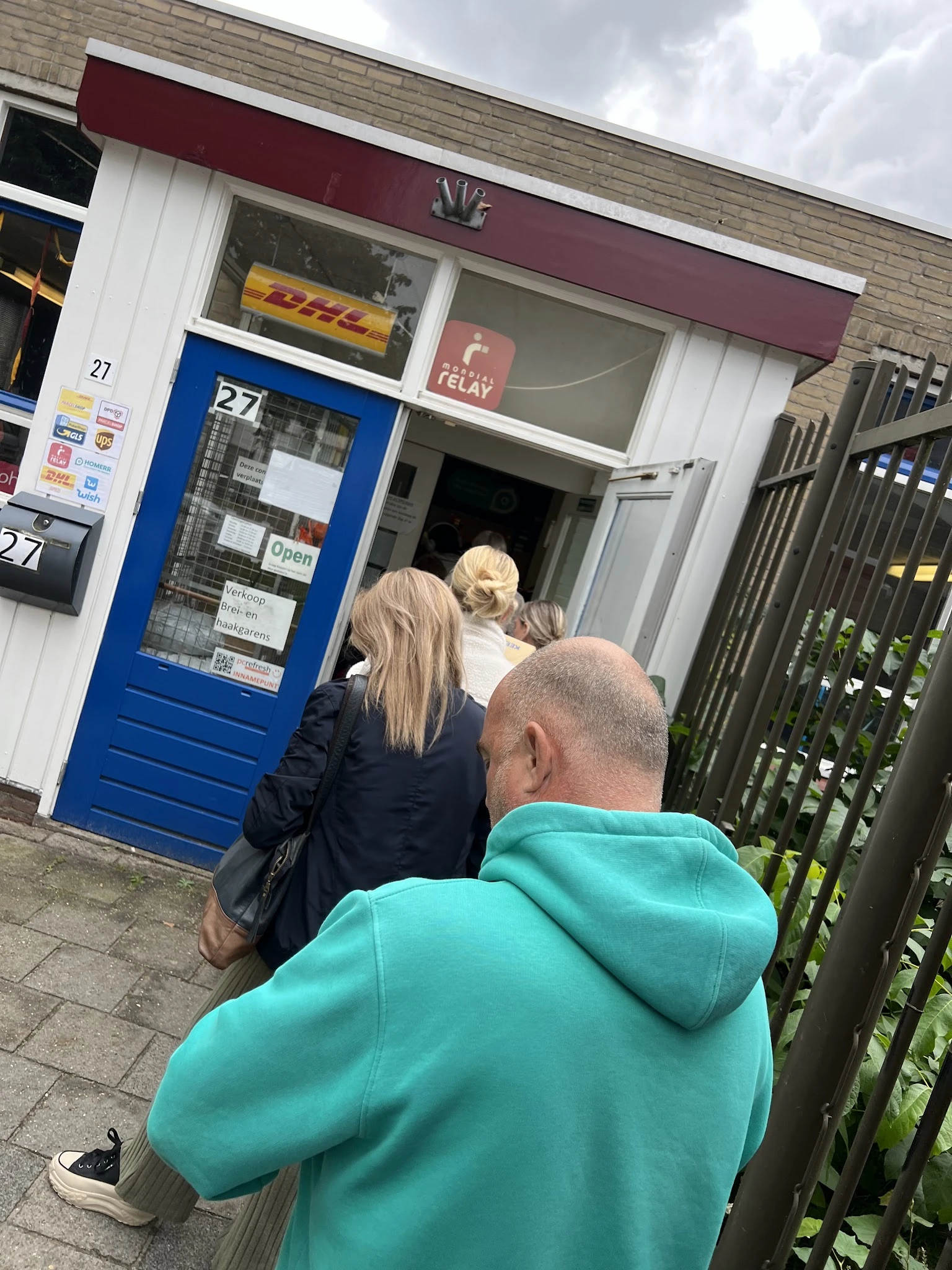 Voorkant van kringloopwinkel met blauwe deur, mensen staan voor de ingang