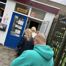 Voorkant van kringloopwinkel met blauwe deur, mensen staan voor de ingang