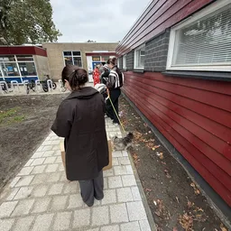 Groep kinderen en volwassenen buiten bij de kringloopwinkel, mogelijk tijdens een activiteit of schoolbezoek