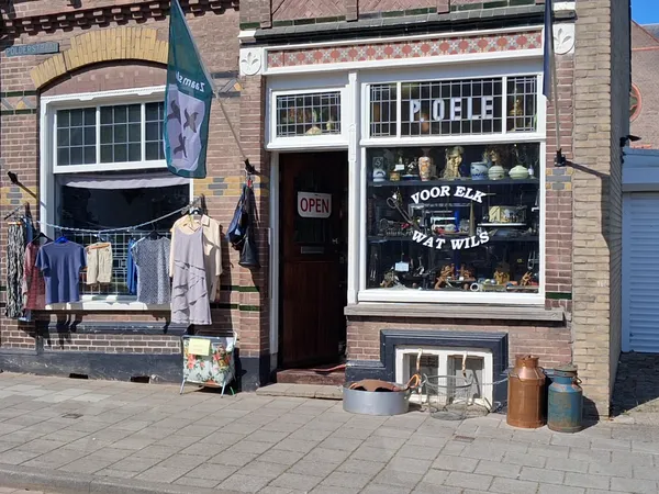 Bakstenen gevel van kringloopwinkel met etalage, deur, raam met spullen en kleding op een waslijn buiten