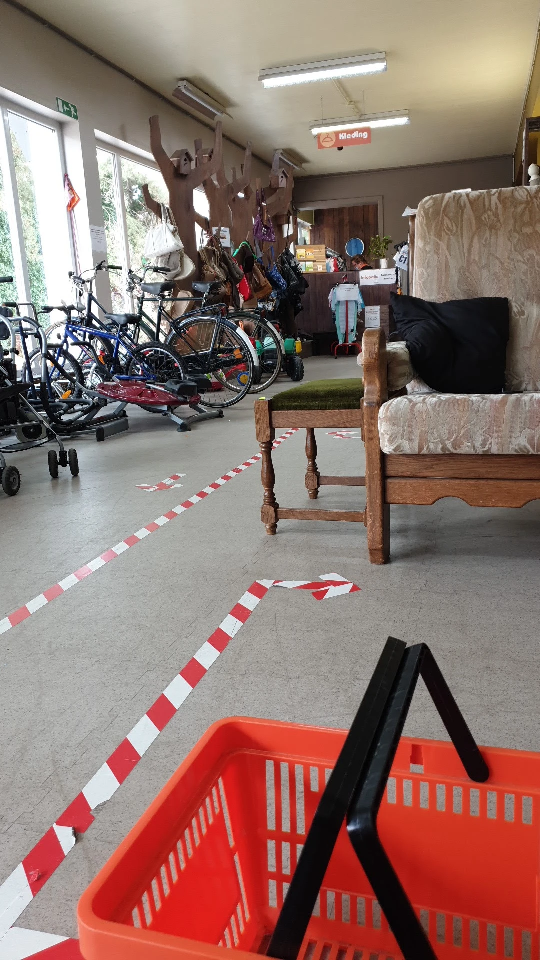 Grijze betonvloer met rood-wit markeringstape en houten stoelen, op de achtergrond fietsen en meubels