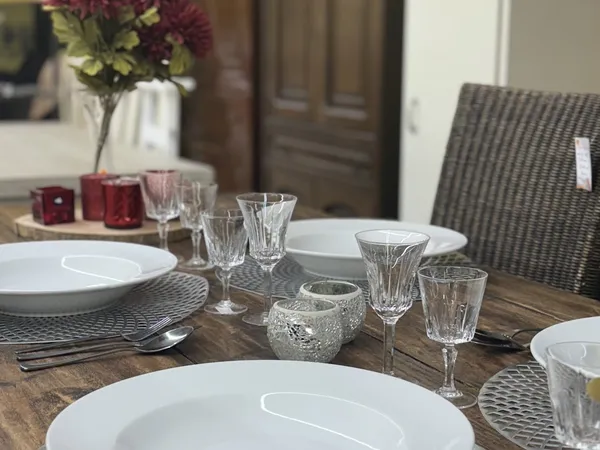 Gedekte eettafel met witte borden, kristallen glazen en bloemenvaas in een ingerichte ruimte