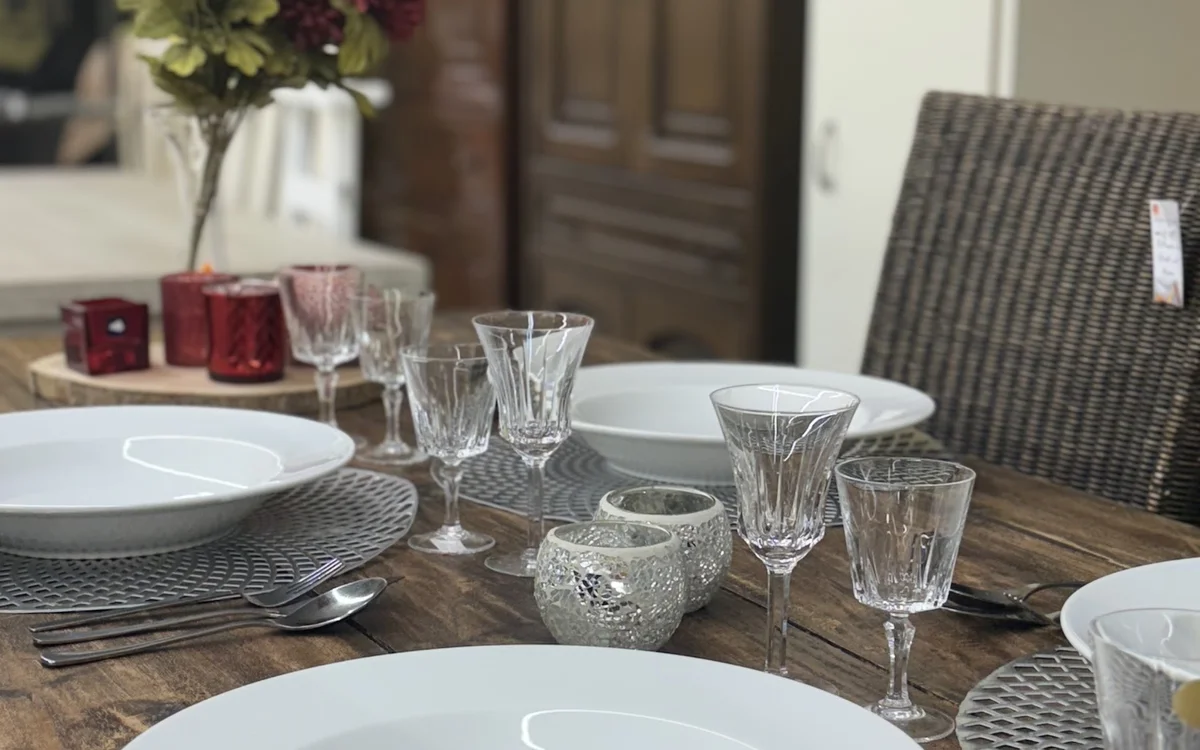 Gedekte eettafel met witte borden, kristallen glazen en bloemenvaas in een ingerichte ruimte