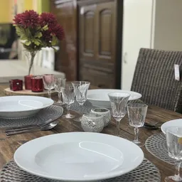 Gedekte eettafel met witte borden, kristallen glazen en bloemenvaas in een ingerichte ruimte