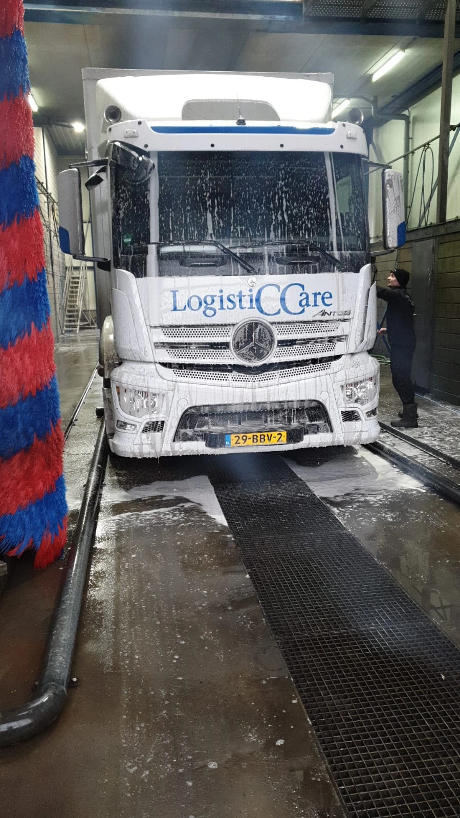 Witte vrachtwagen met LogistiCCare-logo en Nederlandse nummerplaat voor ingang van winkel