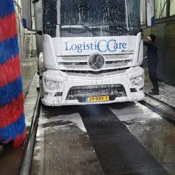 Witte vrachtwagen met LogistiCCare-logo en Nederlandse nummerplaat voor ingang van winkel