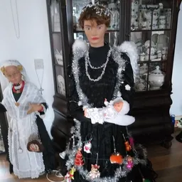 Etalagepop in zwarte jurk met witte bontafwerking en sieraden, achter vitrinekast met servies