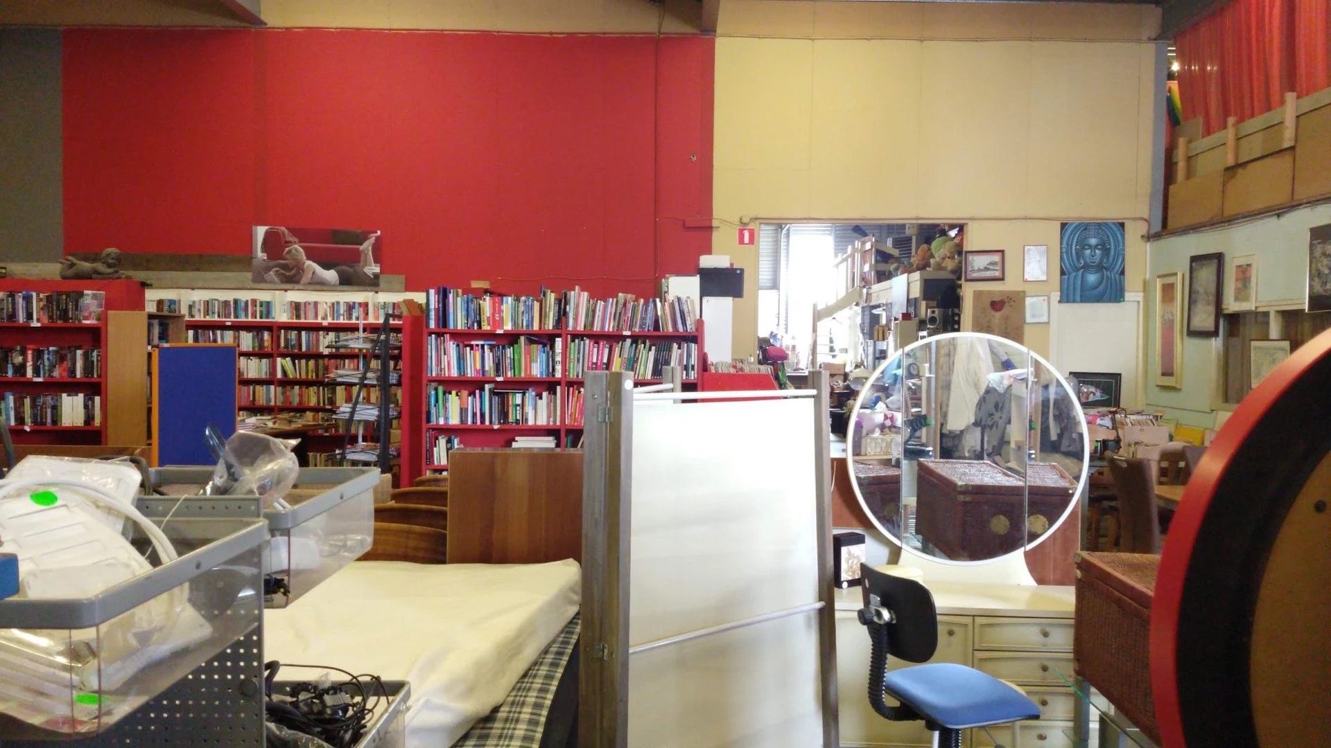 Winkelinterieur met boekenkasten, rode wand, gele wand, koelkast en verschillende meubelstukken