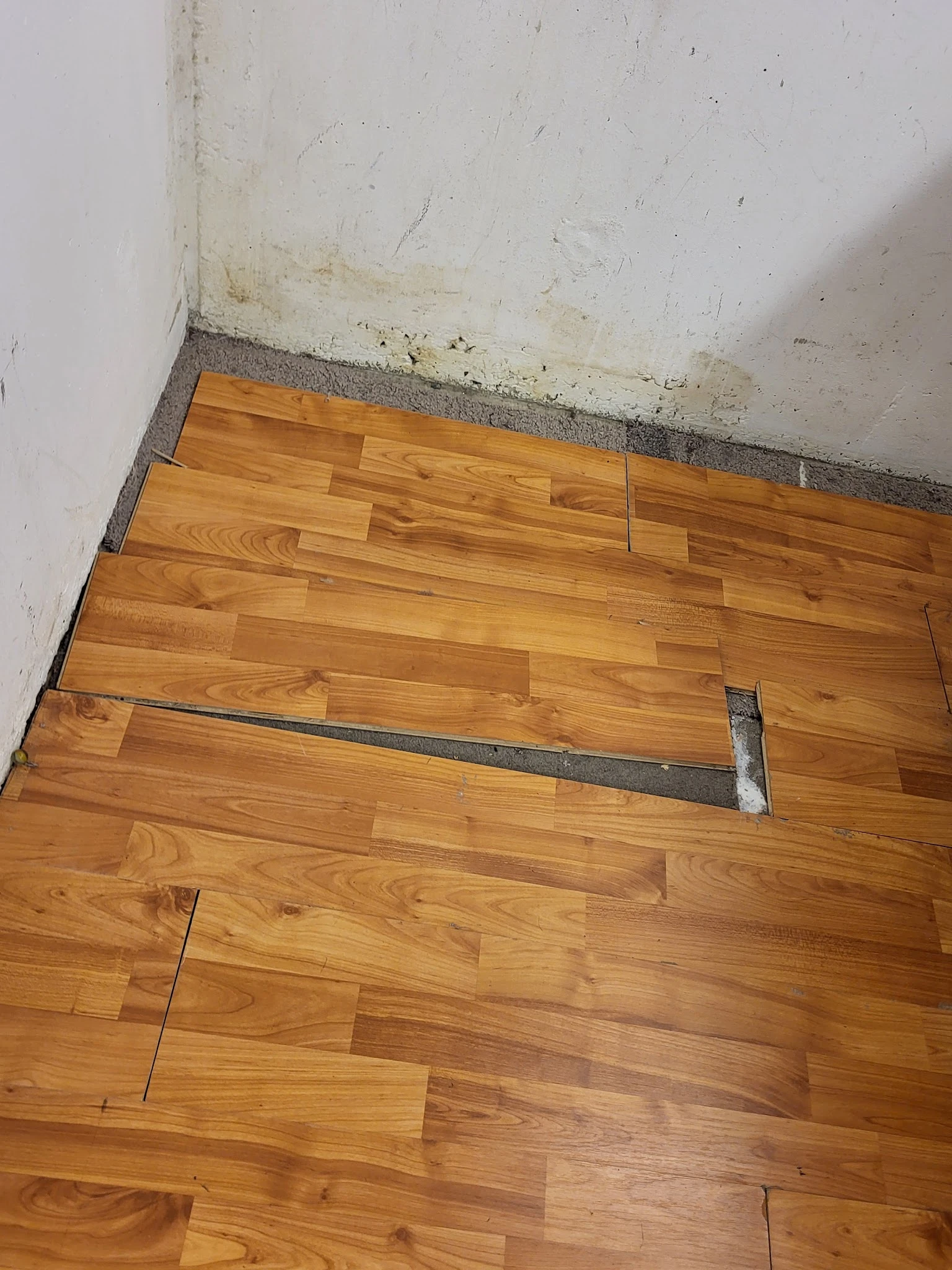 Houten vloer met reparatie en grijze voegband onder witte muur