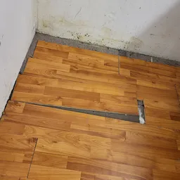 Houten vloer met reparatie en grijze voegband onder witte muur