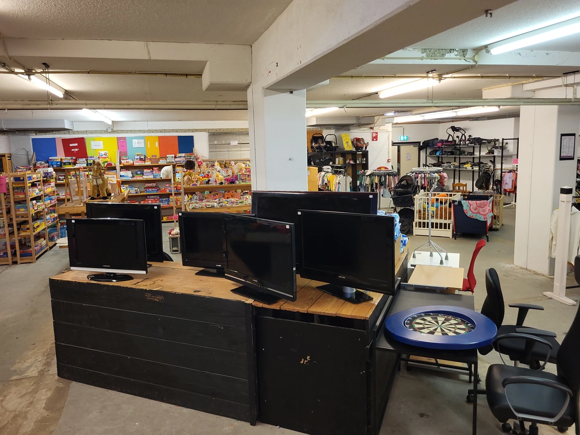 Computerworkstations met drie monitoren en bureaustoel in een kringloopwinkel, met stellingen met spullen op de achtergrond
