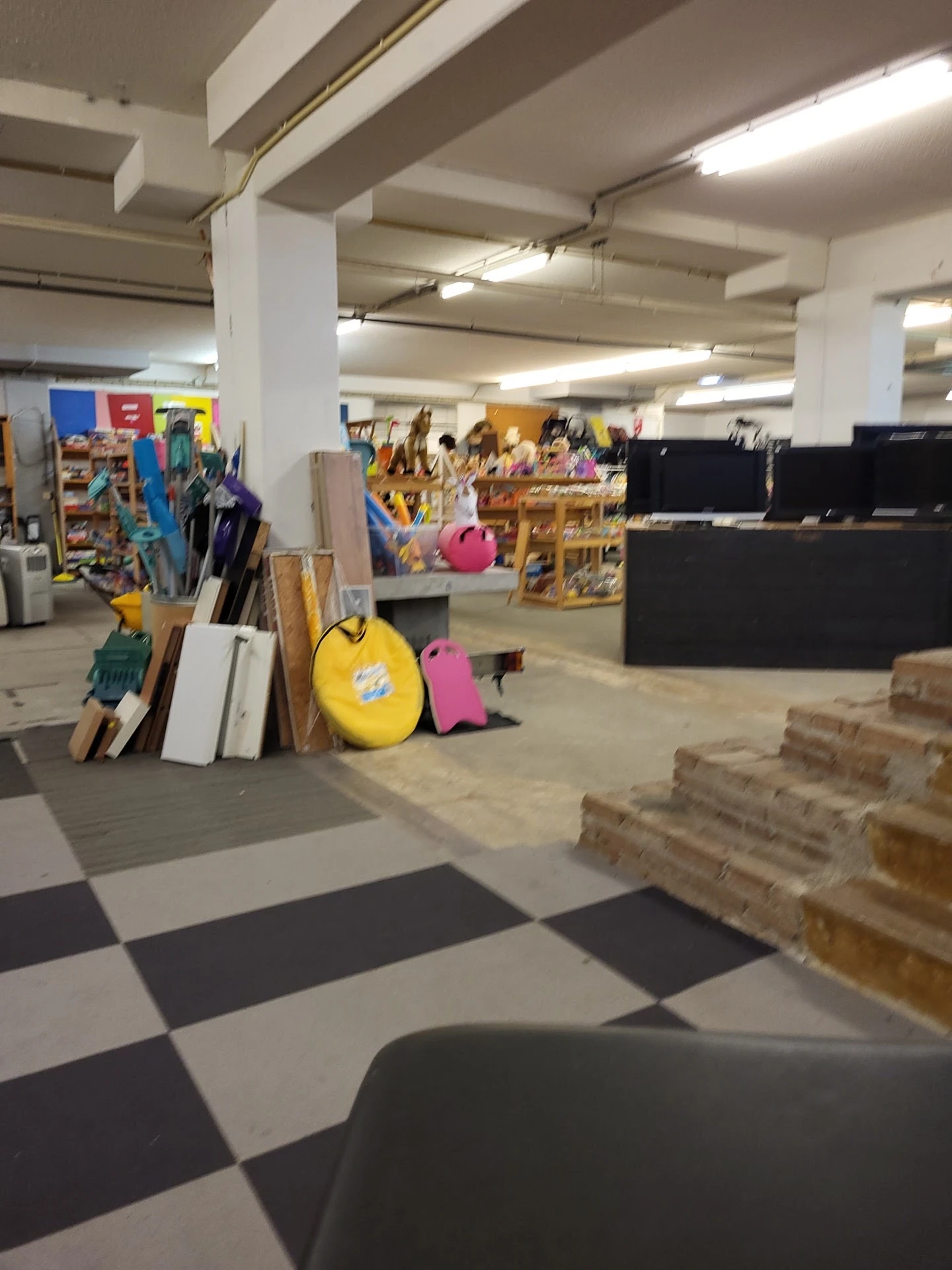 Winkelinterieur met stellingen, dozen, gele bal, gereedschap en diverse spullen op de vloer