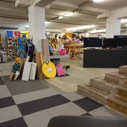 Winkelinterieur met stellingen, dozen, gele bal, gereedschap en diverse spullen op de vloer