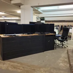 Winkelvloer met zwarte balie, computermonitoren, kledingrekken en stellingen op de achtergrond