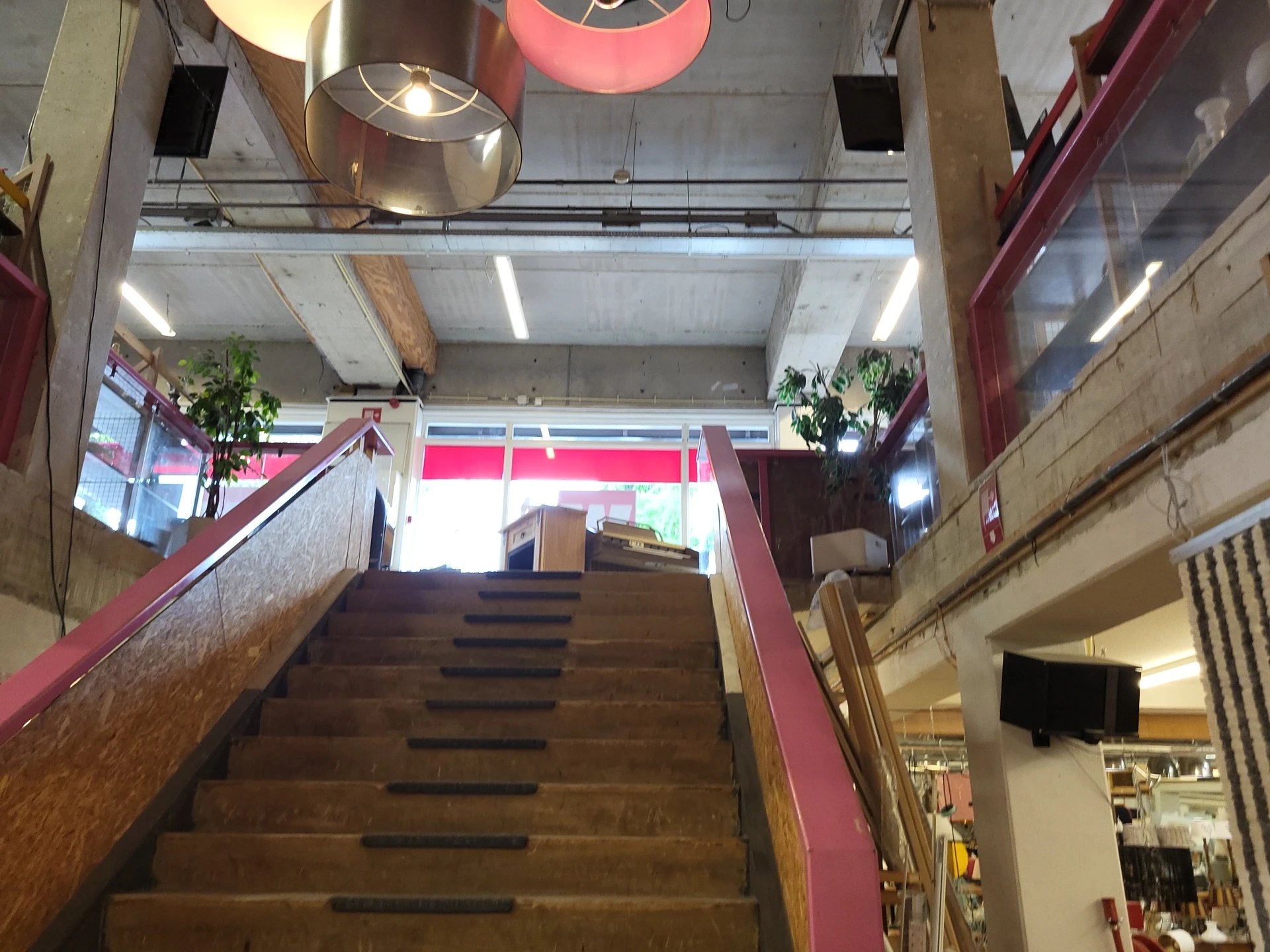 Trappenhuisgedeelte in kringloopwinkel met houten trappen, rode leuningen en winkelinterieur zichtbaar