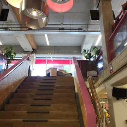 Trappenhuisgedeelte in kringloopwinkel met houten trappen, rode leuningen en winkelinterieur zichtbaar
