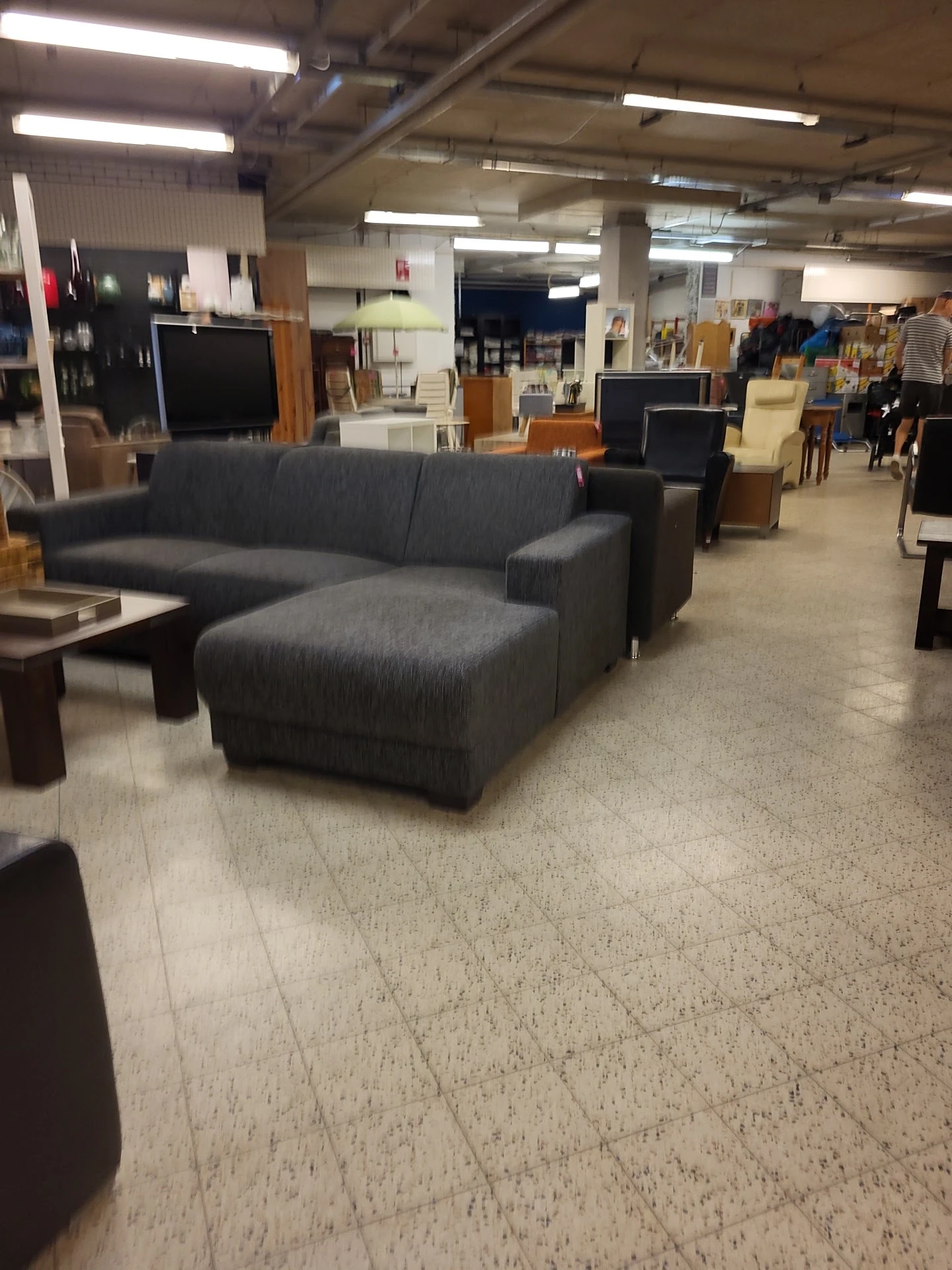 Grijze hoekbank en houten tafels in de winkel, met diverse meubels en spullen op de achtergrond