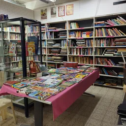 Uitgestalde boeken en strips op een tafel met roze kleed in een boekenkringloop, met boekenkasten op de achtergrond