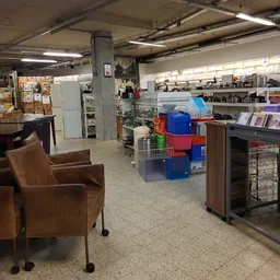 Winkelvloer van kringloopwinkel met stellingen, huisraad, een bruine leunstoel en diverse tweedehands artikelen