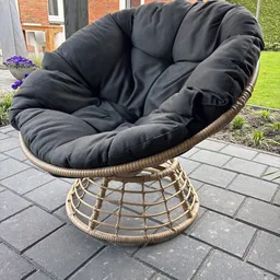 Zwart gestoffeerde rotan hangstoel op terras met grastuin op achtergrond