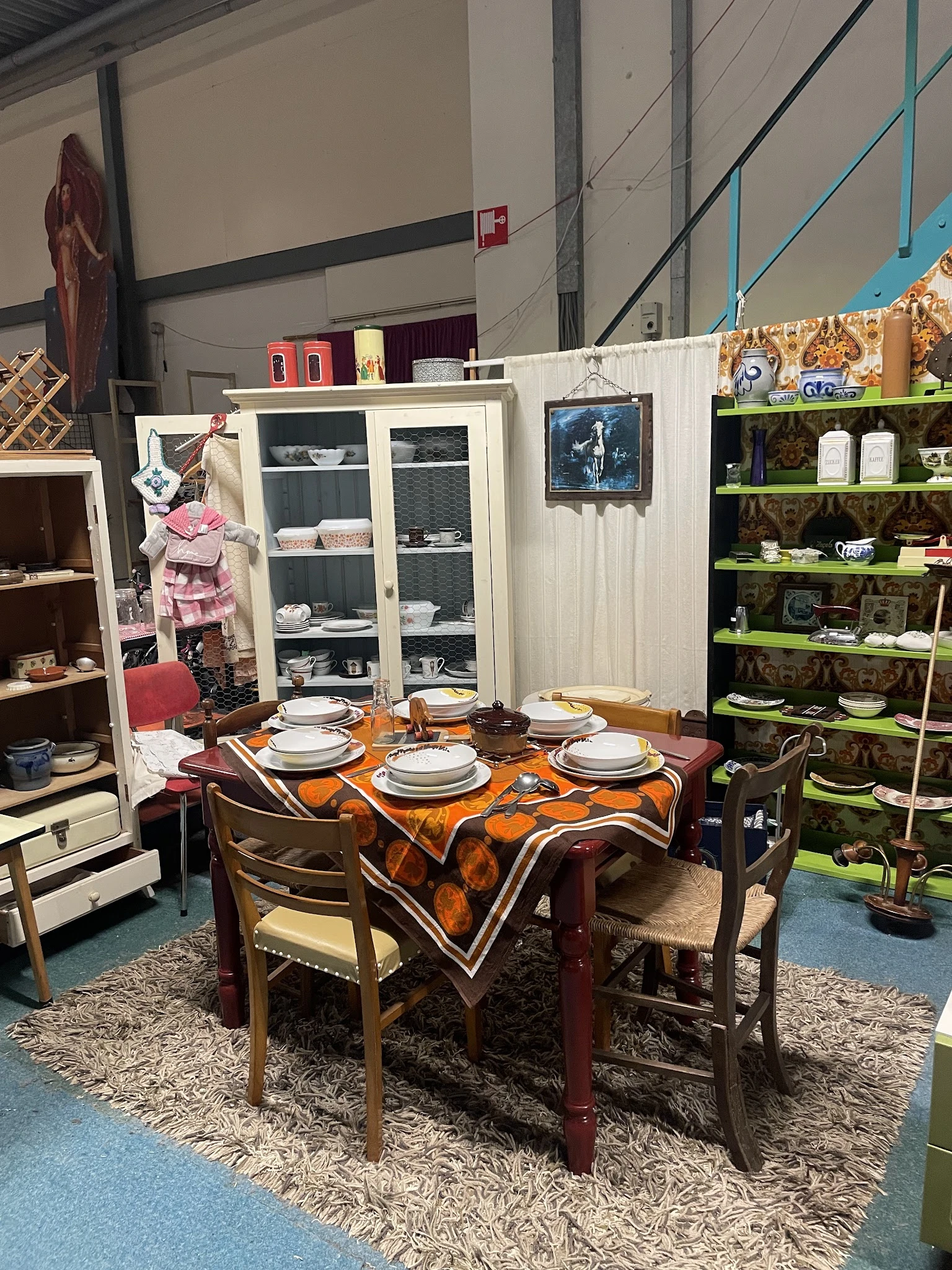 Ingerichte woonkamer in kringloopwinkel met tafel, stoelen, servies en kasten met glazen deuren