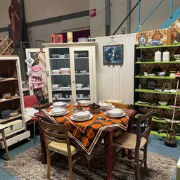 Ingerichte woonkamer in kringloopwinkel met tafel, stoelen, servies en kasten met glazen deuren