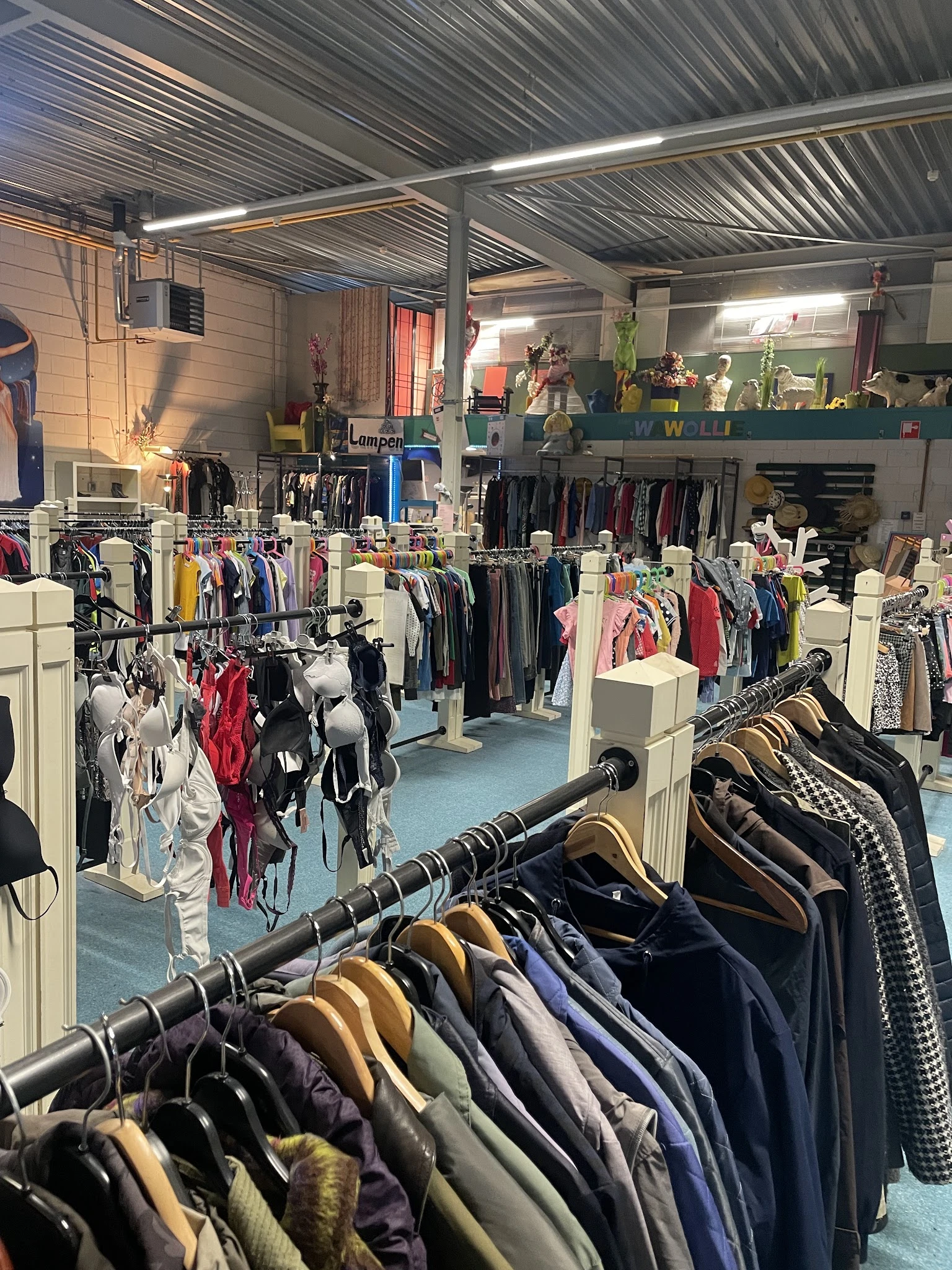 Winkelvloer van kringloopwinkel met rekken vol kleding, witte stellingen en blauwe vloer