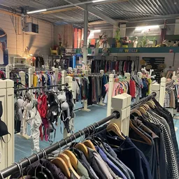 Winkelvloer van kringloopwinkel met rekken vol kleding, witte stellingen en blauwe vloer