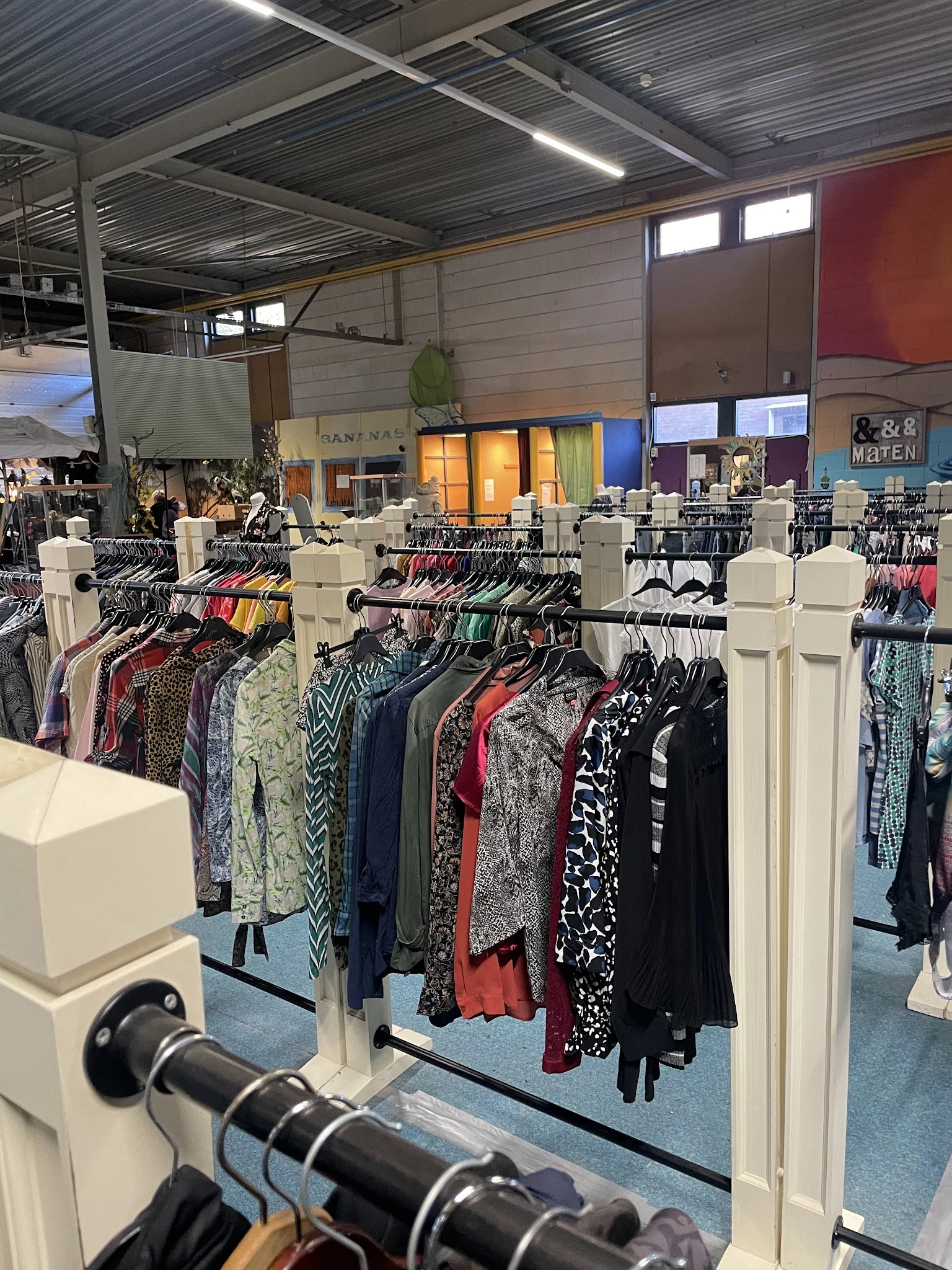 Rekken met tweedehands dameskleding in verschillende kleuren en patronen in de kringloopwinkel