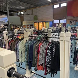 Rekken met tweedehands dameskleding in verschillende kleuren en patronen in de kringloopwinkel
