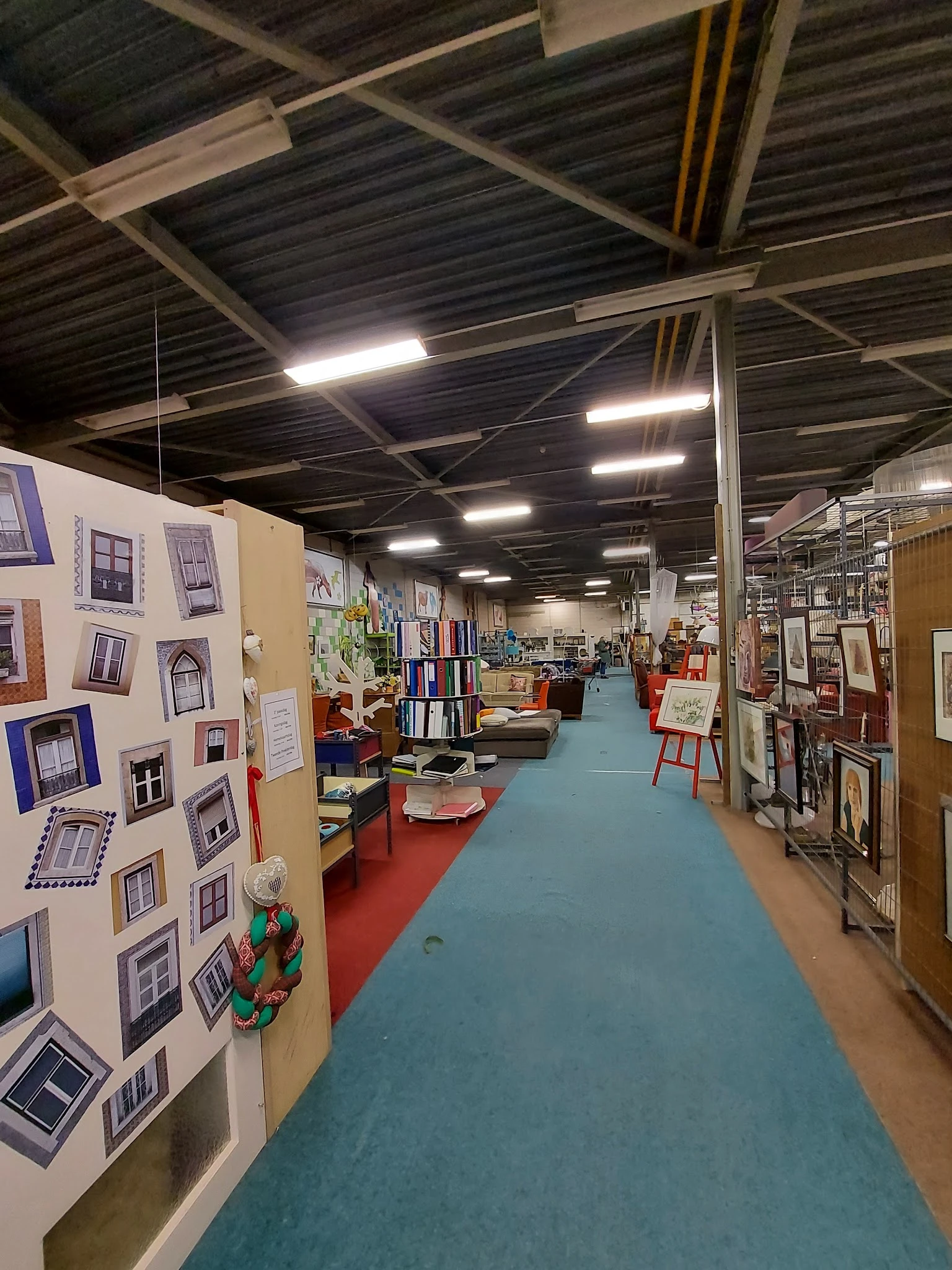 Overzicht van de winkelvloer met gekleurde looppaadjes, stellingen met boeken en diversen spullen, displayborden met ramen en