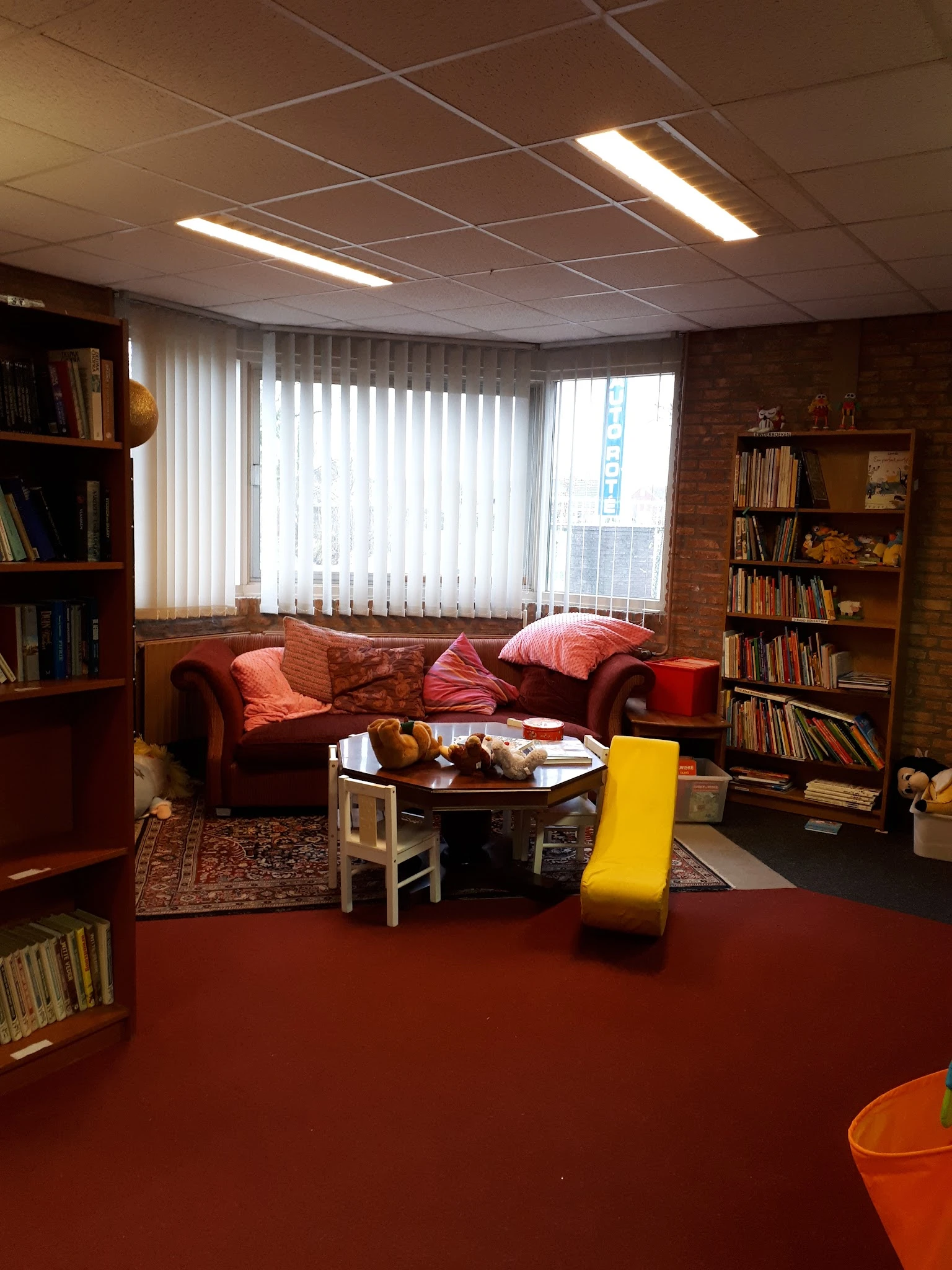 Woonkamer-achtige inrichting met rode bank, boekenkast en gele stoel in kringloopwinkel