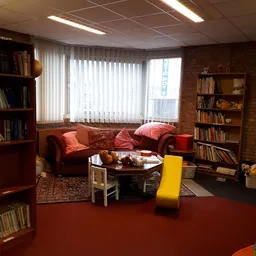 Woonkamer-achtige inrichting met rode bank, boekenkast en gele stoel in kringloopwinkel