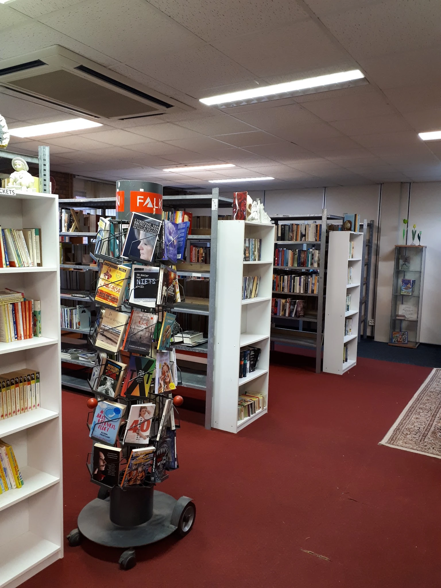 Binnenaanzicht van kringloopwinkel met witte boekenkast, rode vloer en uitgaansmiddelen in het midden