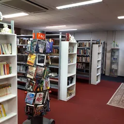 Binnenaanzicht van kringloopwinkel met witte boekenkast, rode vloer en uitgaansmiddelen in het midden