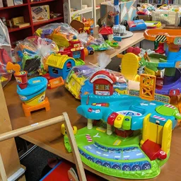 Kinderspeelgoed uitgestald op tafels, waaronder kleurrijke kunststof speelsets, treinen en activiteitenspeeltuigen