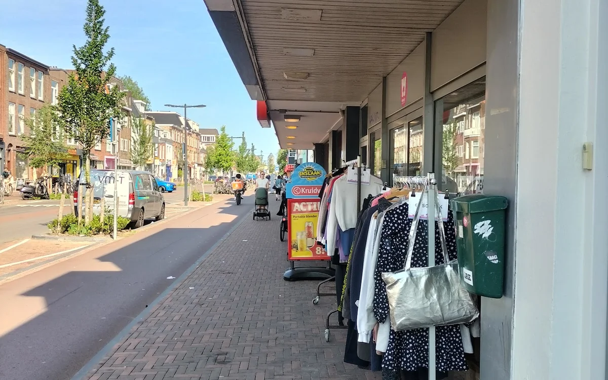 Winkelgevel met uitstallingen kleding aan het raam langs een zonnig winkelstraatje