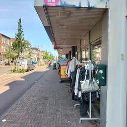 Winkelgevel met uitstallingen kleding aan het raam langs een zonnig winkelstraatje