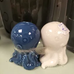 Twee decoratieve keramische poppen, één blauw en één wit, met een takje ertussen