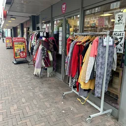 Rekken met tweedehands kleding buiten op het trottoir, waaronder jurken, jassen en sjaals in verschillende kleuren