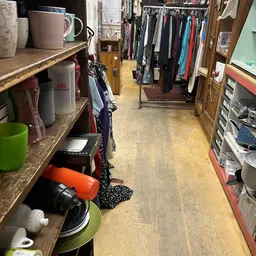 Smalle winkelgang met stellingen aan beide zijden, vol met kleding en huishoudspullen