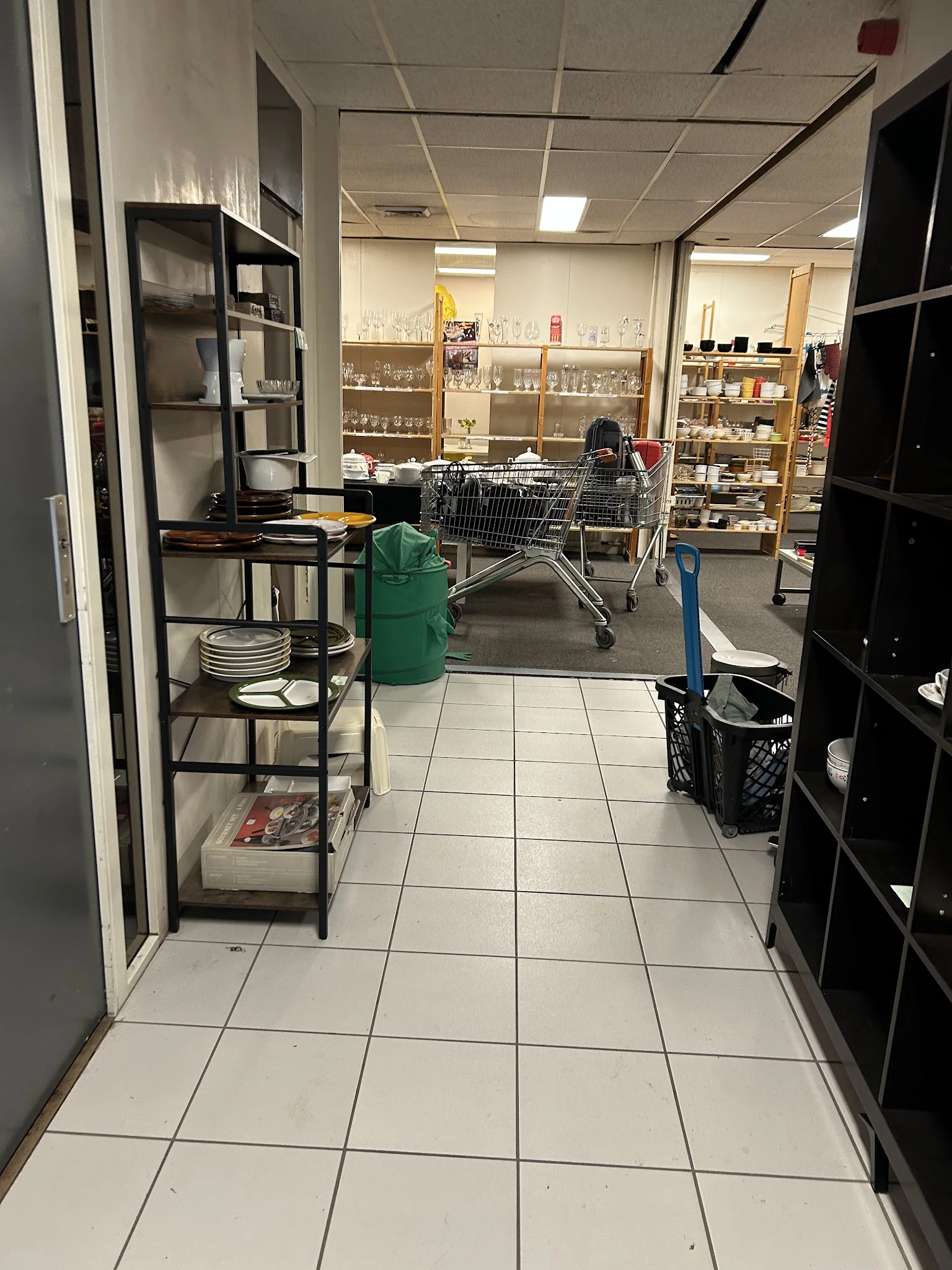 Winkelvloer van kringloopwinkel met winkelwagen, stellingen met serviesgoed en huishoudartikelen